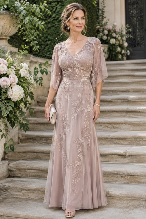 Blush Lace Evening Gown Woman wearing a blush pink floor-length lace gown with sheer flutter sleeves and holding a small clutch on stone steps.