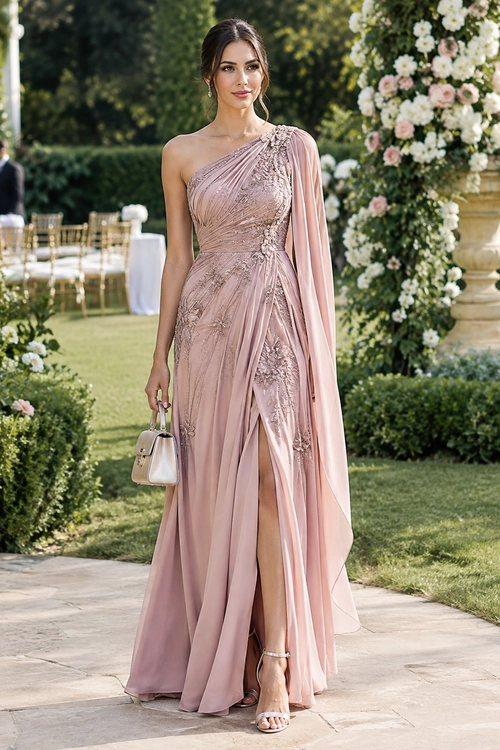 Blush Pink One-Shoulder Gown A woman wears a blush pink one-shoulder embellished gown with a flowing draped sleeve, thigh-high slit, metallic sandals, and a small handbag.