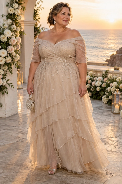 Champagne Off-Shoulder Evening Dress A woman wears a champagne off-shoulder gown with sheer sleeves, sparkling embellishments, layered tulle, a small metallic clutch, and open-toe heels.