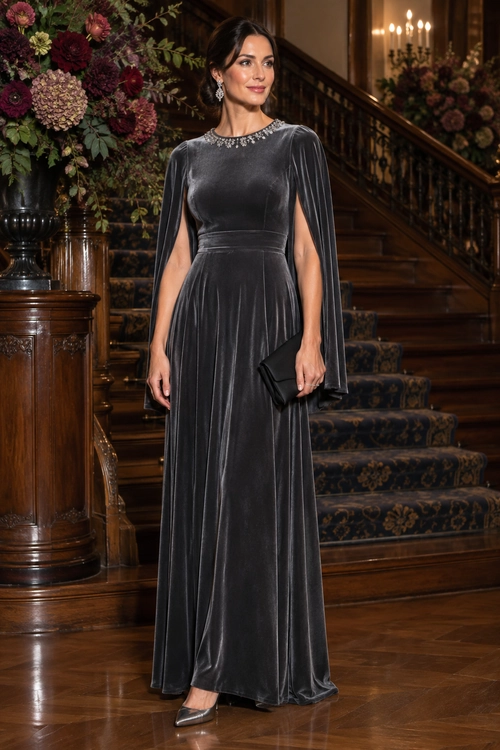 Woman wearing a charcoal velvet floor-length evening gown with cape sleeves, a jeweled neckline, pointed heels, and a black clutch.