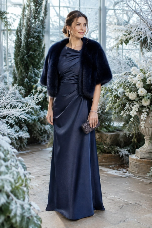 Navy Evening Gown with Fur Wrap Woman wearing a floor-length navy gown with a dark fur wrap and beaded clutch in a winter garden setting.