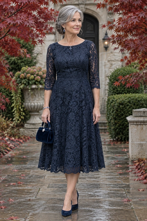 A woman wears a navy lace midi dress with sheer three-quarter sleeves, pointed heels, and a matching handbag in a formal garden setting.
