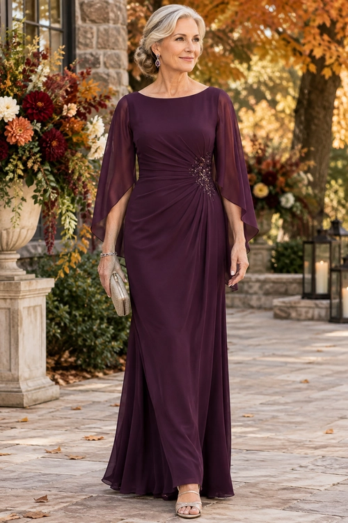 Plum Draped Evening Dress Woman wearing a floor-length plum dress with sheer cape sleeves, a jeweled gathered waist, metallic clutch, and strappy sandals.