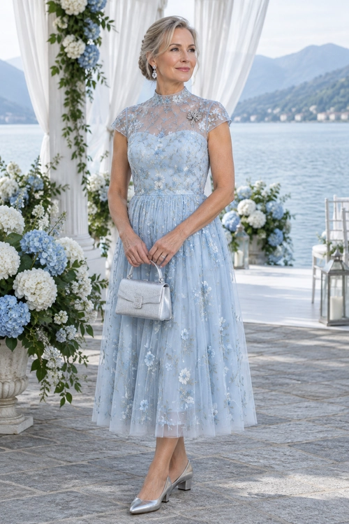 Powder Blue Floral Midi Dress Woman wearing a powder blue floral lace midi dress with silver pointed-toe pumps and a matching silver clutch.