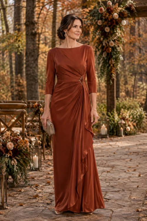 Woman wearing a rust-colored long-sleeve floor-length gown with draped ruching, a jeweled waist detail, and a small clutch.