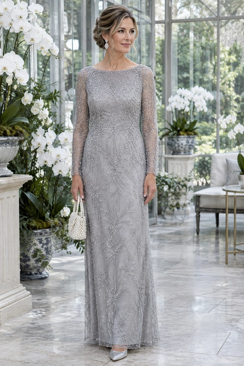 Woman wearing a floor-length silver-gray embellished gown with sheer long sleeves, drop earrings, a beaded white handbag, and pointed heels.