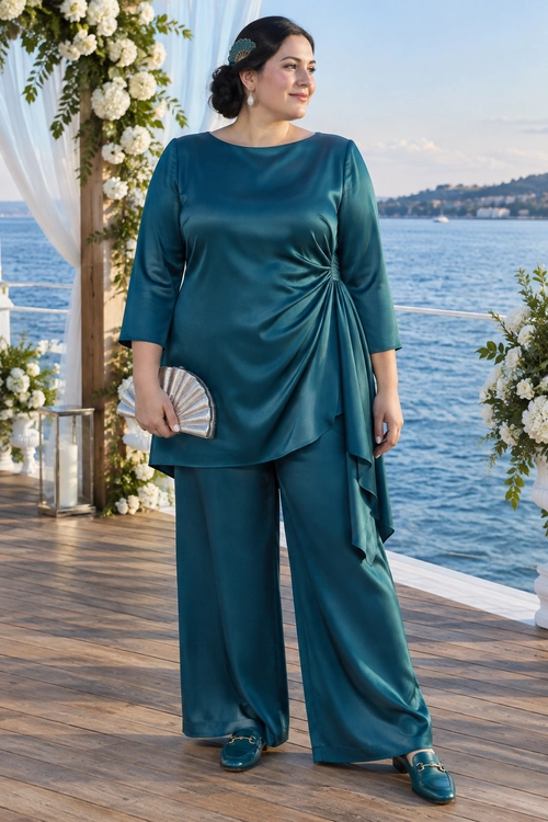Teal Draped Satin Pantsuit Woman wearing a teal satin tunic with draped side detail, wide-leg trousers, matching loafers, and a silver fan clutch.